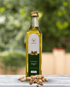 The Deep Soil Cold-Pressed Groundnut Oil 500ml glass bottle with a pile of whole peanuts on a marble surface and blurred nature background